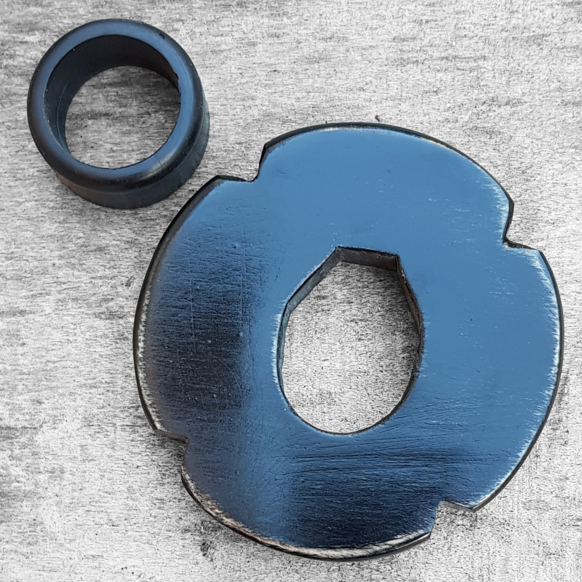 A wooden tsuba, shaped like a four-leaf petal, next to a rubber stopper, placed on a wooden surface.