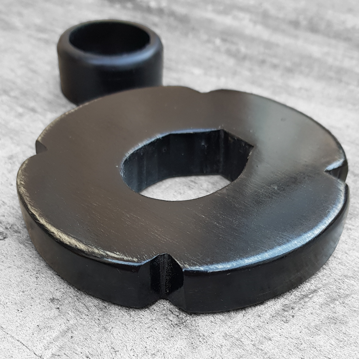 A wooden tsuba, shaped like a four-leaf petal, next to a rubber stopper, placed on a wooden surface.