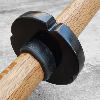 A wooden tsuba, shaped like a four-leaf petal, next to a rubber stopper, placed on a wooden surface.