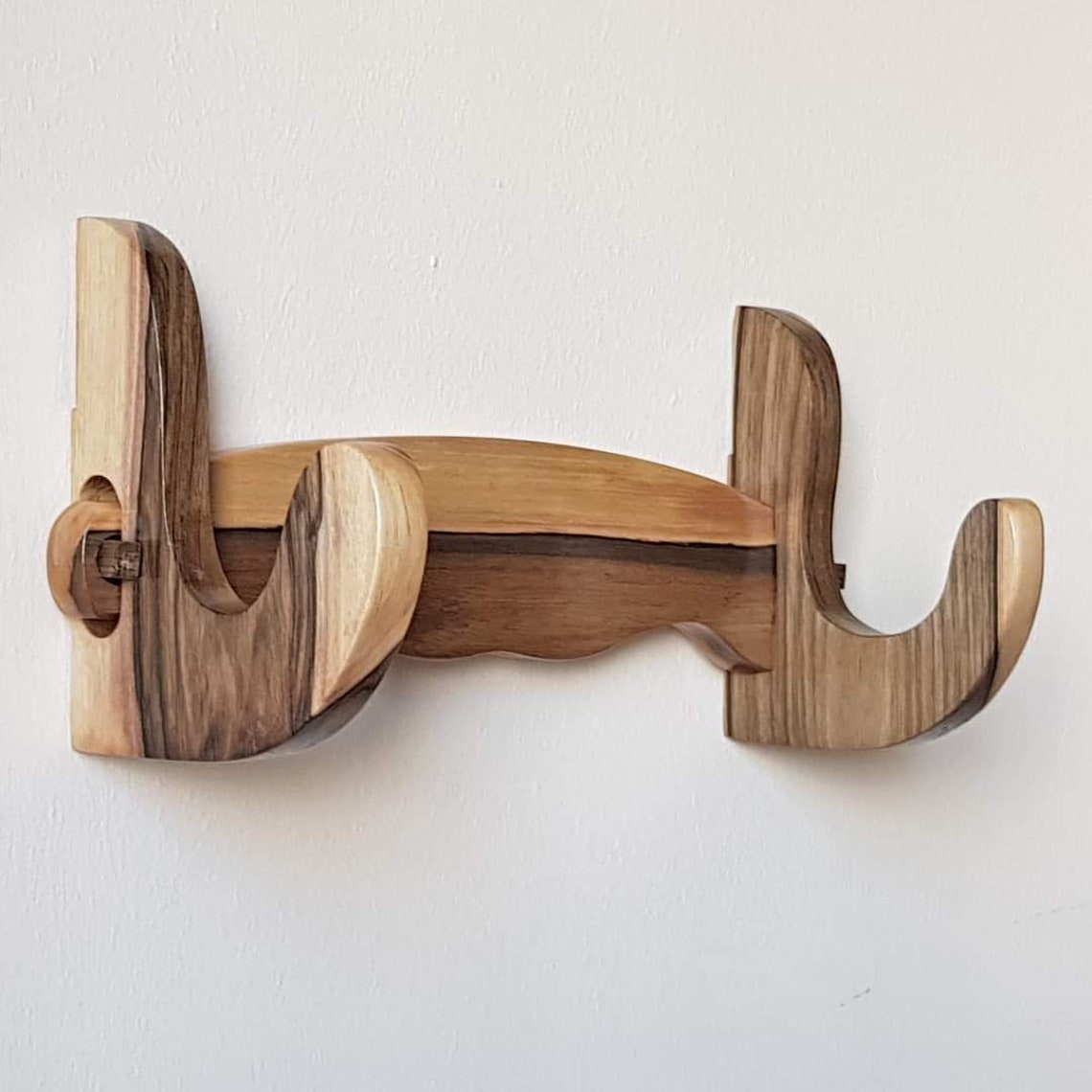 A wall mounted wooden rack designed to hold a sword, ax, or rifle, featuring a natural walnut finish.